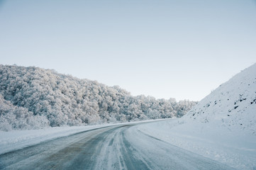 Snow road and car tracks on the road in the winter in the North Caucasus. Snow-covered trees and mountains. The concept of winter travel by car