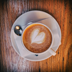 hot cappuccino coffee with heart shaped froth on wooden table