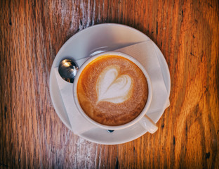 hot cappuccino coffee with heart shaped froth on wooden table