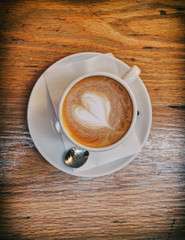 hot cappuccino coffee with heart shaped froth on wooden table