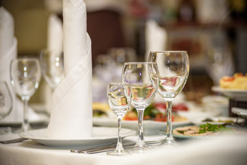 Glasses, forks, knives, napkins and decorative flower on a table served for dinner in cozy restaurant.