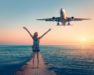 Airplane and woman at sunset. Summer landscape with girl standing on the sea pier with raised up...