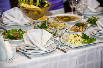 Glasses, forks, knives, napkins and decorative flower on a table served for dinner in cozy restaurant.