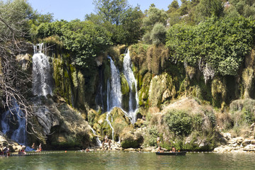 Fototapeta na wymiar Kravica waterfalls in Bosnia Herzegovina, with few people bathing under it