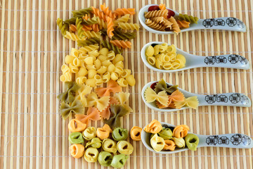 Pasta in porcelain spoons on bamboo