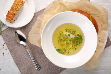 chicken soup with bread in white plate on a white wooden background
