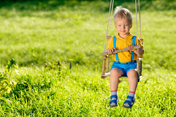Rural scene with toddler boy swinging outdoors.