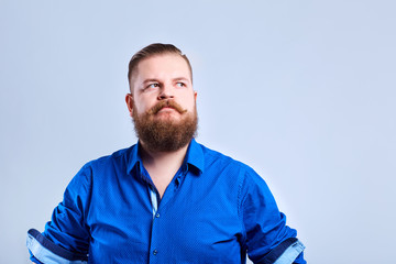 A fat, bearded man looks at the gray background with a serious expression of emotion.