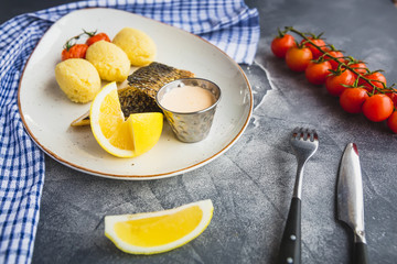 Fish dish with millet porridge, tomato, lemon slice and shrimp sauce on dark table