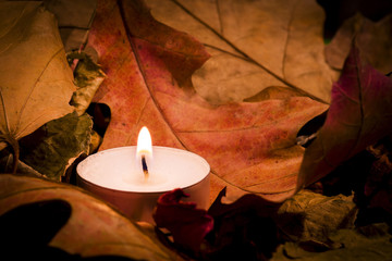 Lighted candle on the background of a large number of wilted leaves