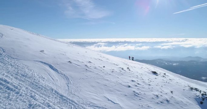Side aerial over people hiking with snowshoes on rise in winter snowy mountain ski track field.Sunny day Alps mountains active sport people.4k drone flight establishing shot