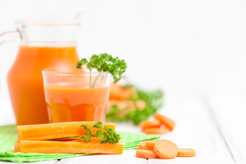 Carrot juice in beautiful glasses, cut orange vegetables and green parsley on white wooden background. Fresh orange drink. Close up photography. Selective focus. Horizontal banner