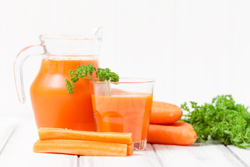 Carrot juice in beautiful glasses, cut orange vegetables and green parsley on white wooden background. Fresh orange drink. Close up photography. Selective focus. Horizontal banner