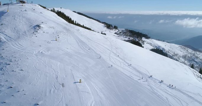 Forward aerial top view over winter snowy mountain ski track field with people in sunny day.Above Alps mountains snow season establisher.4k drone flight establishing shot