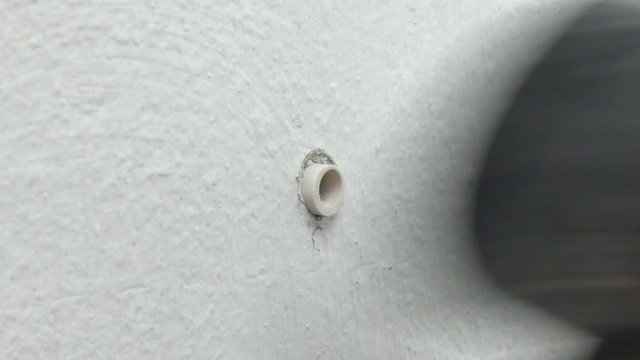 Close up shot hand of man insert plastic cleat in to the hold of cement concrete white wall and using hammer to hit it