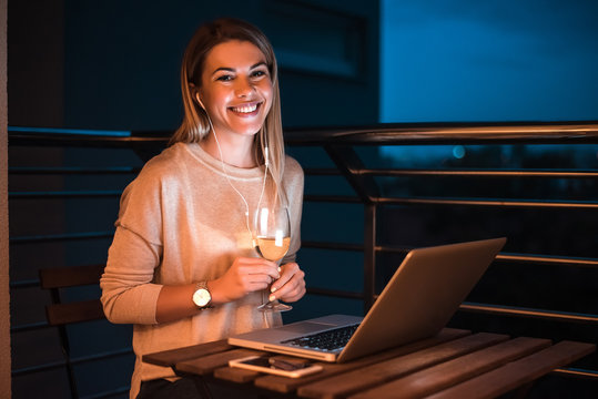 Portrait of blonde woman sitting in balcony with laptop. High ISO image.