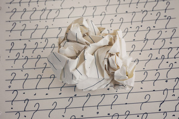 Crumpled paper ball and question marks on sheet of lined paper