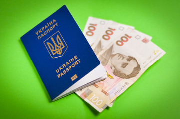 One blue biometric ukrainian foreign passport with gold color inscription and coat of arms on green background and three banknotes of one hundred hryvnias. Travel concept