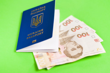 One blue biometric ukrainian foreign passport with gold color inscription and coat of arms on green background and three banknotes of one hundred hryvnias. Travel concept