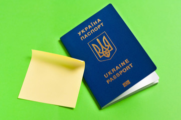 One blue biometric ukrainian foreign passport with gold color inscription and coat of arms on green background and yellow stickky blank sticker