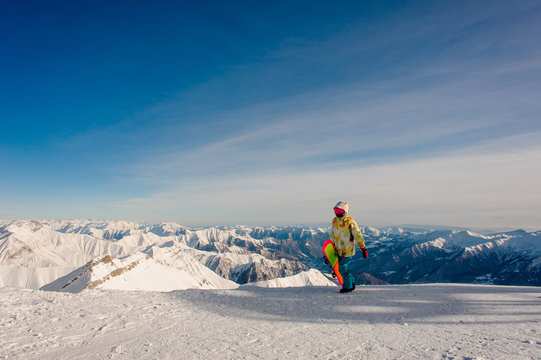 Female snowboarder in sportswear walking on the mountain peak