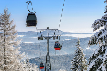 Gondola cabin lift in the ski resort over the forest on the background of snowy mountains in sunny day (high details) © WDnet Studio