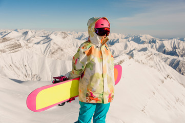 Female snowboarder in sportswear standing on the mountain peak