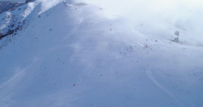 Side aerial over winter snowy mountain top ski tracks resort with skier people skiing.Sunny day,foggy clouds.Fog rising.Alps mountains snow season establisher.4k drone flight sport establishing
