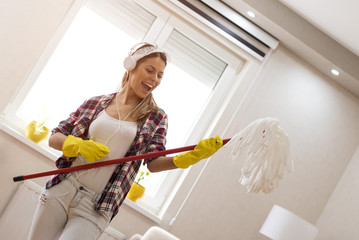 Young woman with headphones and mop ready for home cleaning