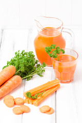 Carrot juice in beautiful glasses, cut orange vegetables and green parsley on white wooden background. Fresh orange drink. Close up photography. Selective focus. Vertical banner