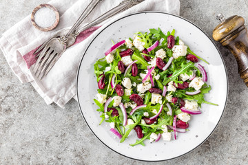 A plate of nutritious simple salad with arugula, beans, soft cheese, onions and oil