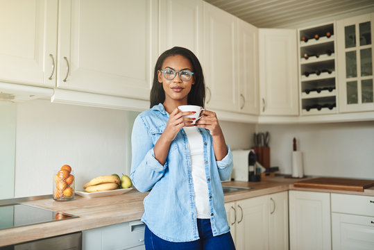 Smiling African Woman Leaning On Her Kitchen Counter Drinking Coffee