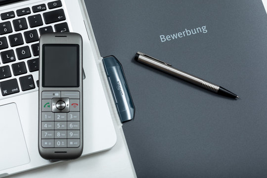 Telefoninterview - Nahaufnahme Bewerbungsmappe mit Telefon, Laptop und Kugelschreiber