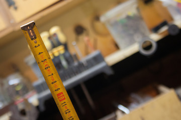 Marco focus is set on the yellow measuring tape.Workshop and tools in the background.