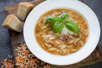 Close-up of italian soup with red lentil, pasta and addition of parmesan served in a white plate, studio shot, selective focus