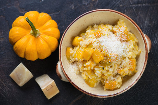 Bowl of pumpkin risotto with parmesan cheese on a dark brown stone background, view from above, horizontal shot