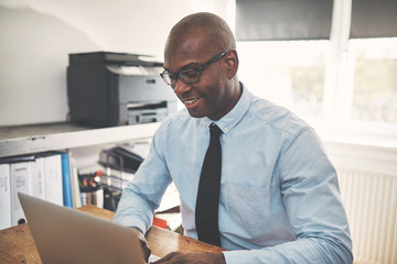 Naklejka premium Smiling African businessman working on a laptop in his office