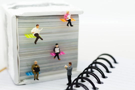 Miniature people: businessman reading newspaper on a big book. Image use for background education or business concept.