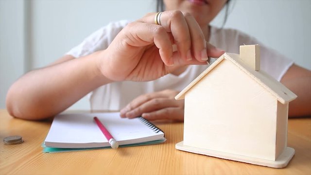 Hands of woman putting coin to House piggy bank saving money for buy home concept