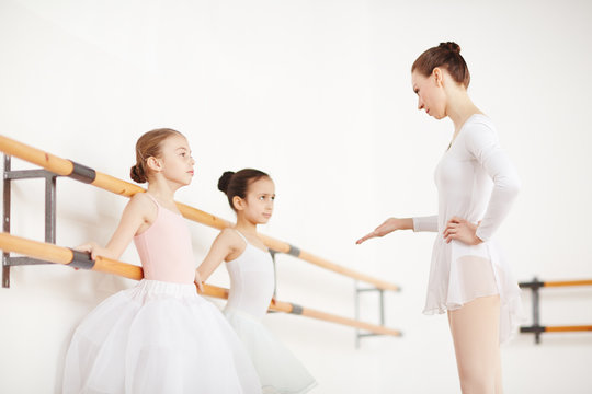 Professional ballet teacher talking to one of little ballerinas during training in classroom