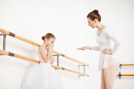 Strict ballet teacher expressing her dissatisfaction while talking to upset little ballerina