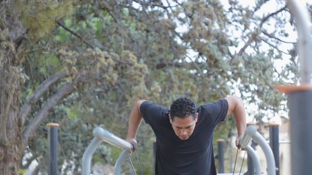 Street workout training. Hispanic man doing parallel bar dips with resistance band on fitness outdoor gym in the park