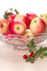 Ripe apples in a crystal vase and rose hips
