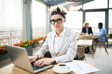 Pretty young blond businesswoman wearing headband, eyeglasses and elegant suit in cafe