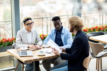 Young man with papers explaining new terms of business contract to his colleagues during negotiation