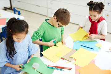 Group of scholars cutting various shapes from green and yellow paper at lesson
