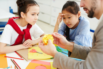 Obraz premium Two serious girls looking at yellow paper snowflakes in hands of their teacher