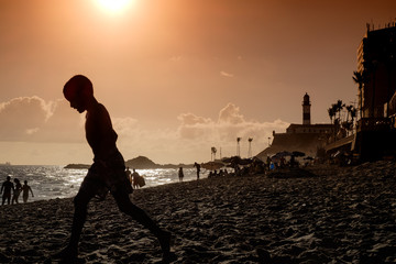Beach life on an urban beach in Salvador de Bahia, Brazil just before sunset. A boy is passing by.