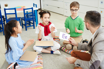 Three schoolkids sitting on the floor and playing english alphabet with teacher