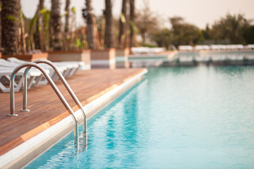 Obraz na płótnie Canvas Empty hotel water pool with turquoise colour water at sunrise, focus on metal hand railing of staircase, copy space, place for text/ Relaxation, summer, vacation and water - concept/ 